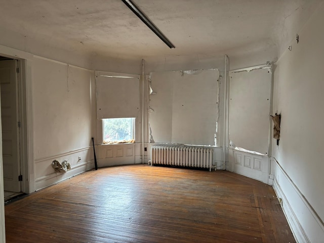 unfurnished room featuring hardwood / wood-style flooring, radiator heating unit, and a decorative wall