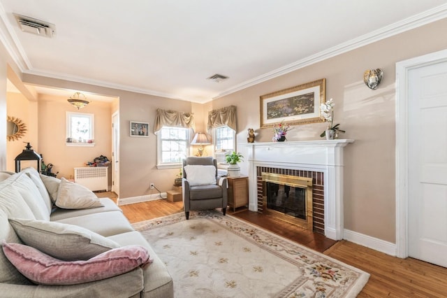 living room featuring visible vents, radiator, a fireplace, and wood finished floors