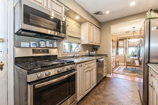 kitchen with visible vents, dark tile patterned flooring, cream cabinetry, a sink, and stainless steel appliances