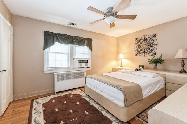 bedroom with visible vents, wood finished floors, radiator heating unit, cooling unit, and baseboards