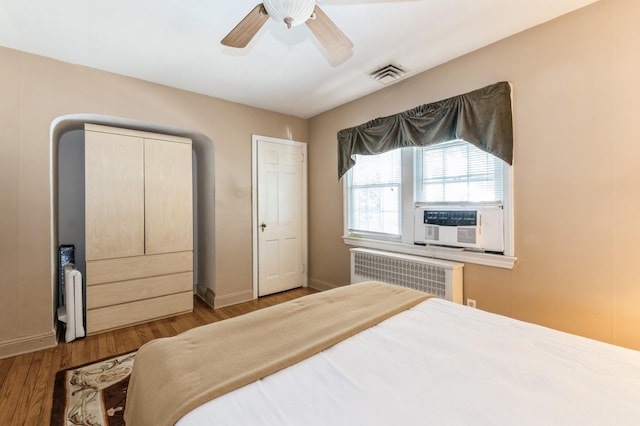 bedroom with visible vents, radiator, baseboards, wood finished floors, and a ceiling fan