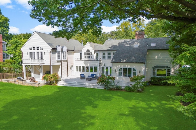 rear view of property with a balcony, a lawn, and a chimney