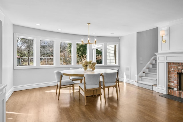 dining area with baseboards, a brick fireplace, wood finished floors, and an inviting chandelier