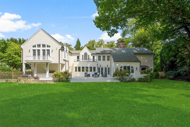 rear view of property featuring a balcony, a lawn, fence, and a chimney