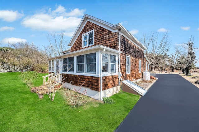 view of side of home featuring a sunroom, aphalt driveway, and a yard