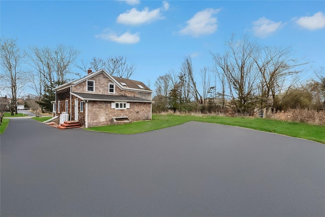 view of home's exterior featuring aphalt driveway, a lawn, and a chimney