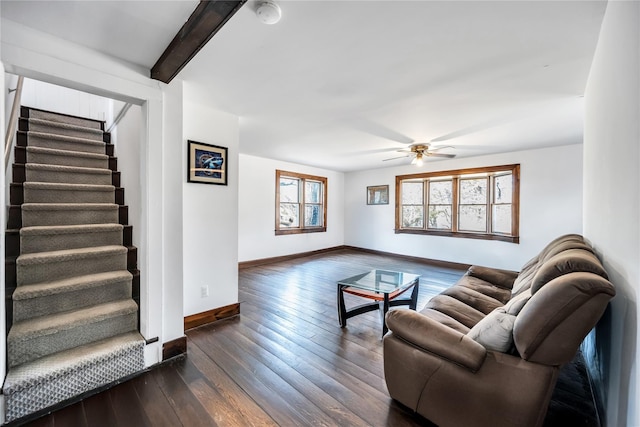 living room featuring dark wood-type flooring, a ceiling fan, beamed ceiling, baseboards, and stairs