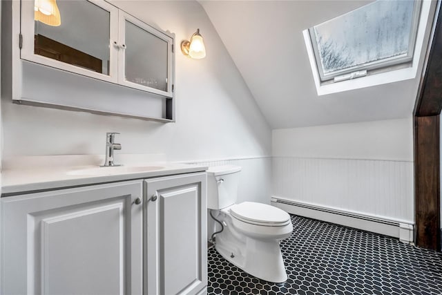 bathroom featuring toilet, vanity, baseboard heating, wainscoting, and lofted ceiling with skylight