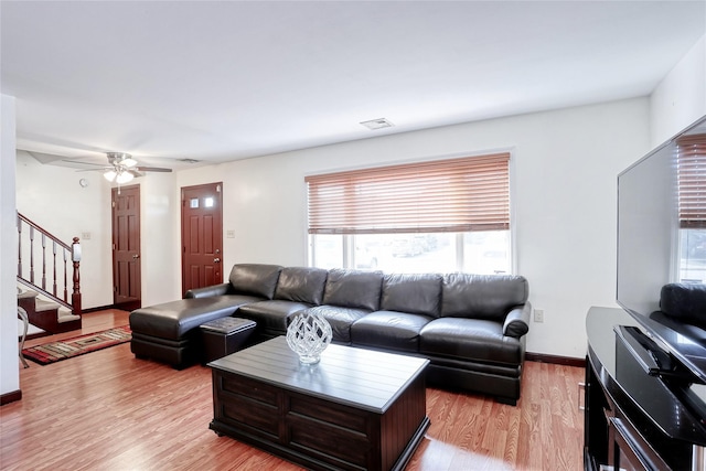 living room with visible vents, ceiling fan, baseboards, light wood-type flooring, and stairs