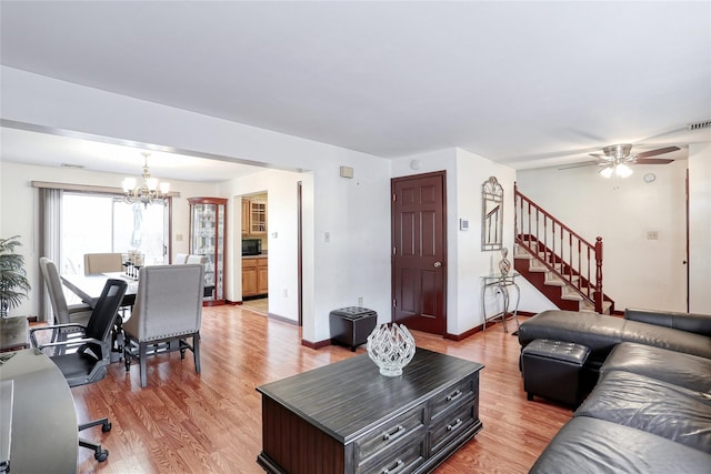 living area featuring stairway, ceiling fan with notable chandelier, baseboards, and light wood-style floors