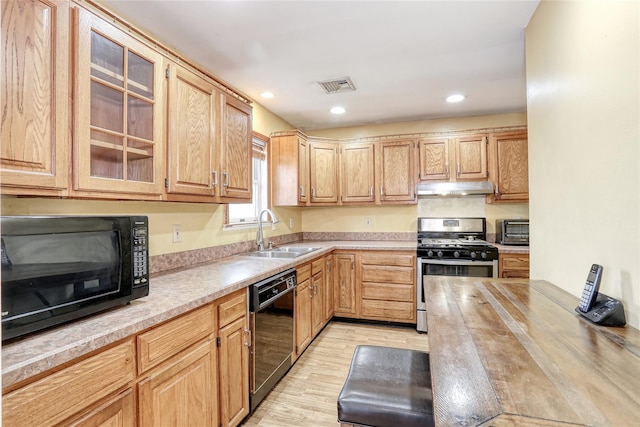 kitchen featuring a toaster, a sink, black appliances, under cabinet range hood, and light wood-type flooring