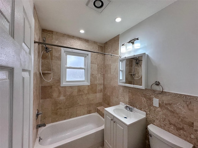 bathroom featuring tile walls, toilet, vanity, and  shower combination