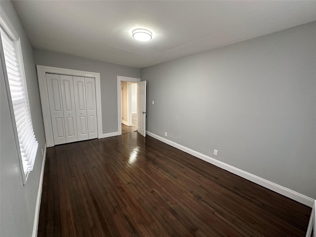 unfurnished bedroom featuring dark wood finished floors, baseboards, and a closet