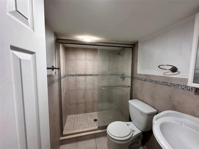 full bath with toilet, a stall shower, a sink, tile walls, and tile patterned flooring