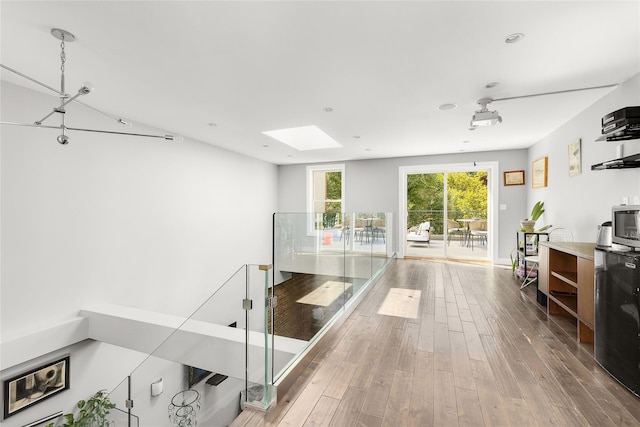 hallway featuring an upstairs landing, baseboards, wood finished floors, and a skylight