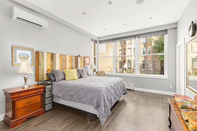 bedroom with an AC wall unit, a baseboard heating unit, baseboards, and wood finished floors