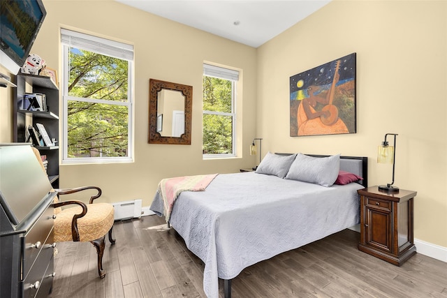 bedroom featuring a baseboard heating unit, wood finished floors, and baseboards