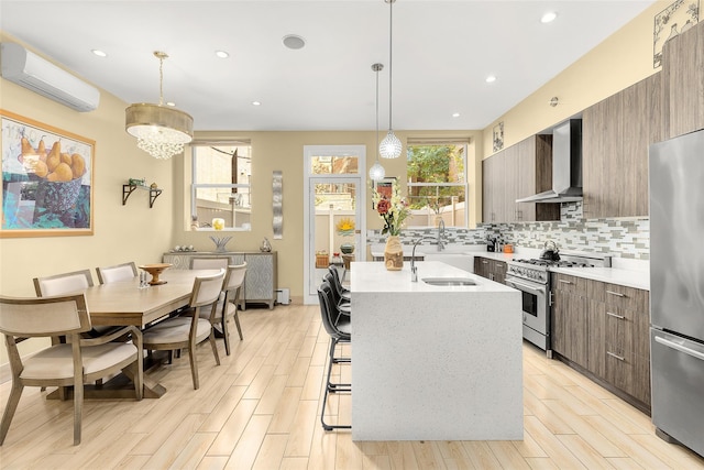 kitchen with wall chimney range hood, appliances with stainless steel finishes, modern cabinets, a wall mounted AC, and a sink