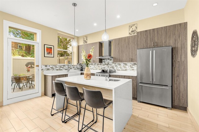 kitchen featuring wall chimney range hood, backsplash, light countertops, and freestanding refrigerator