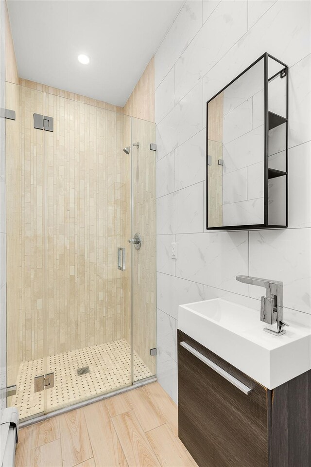 full bathroom featuring vanity, wood finished floors, a stall shower, tile walls, and baseboard heating