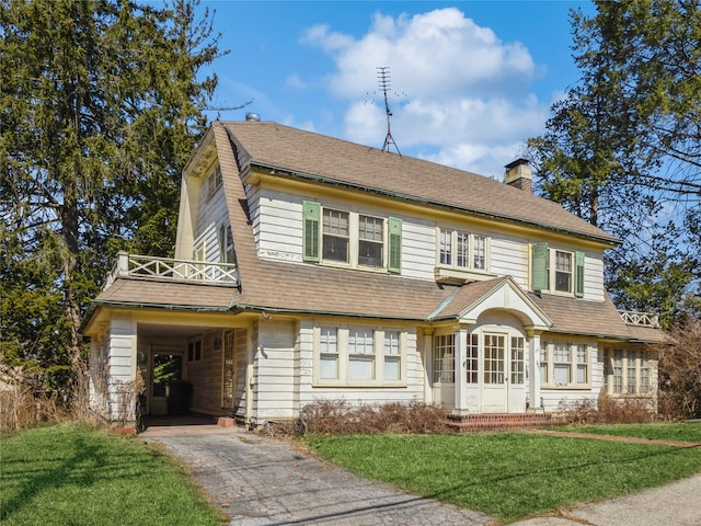 view of front of home with an attached carport, a front yard, roof with shingles, a chimney, and aphalt driveway