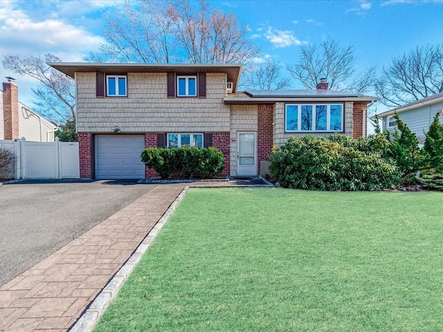 split level home with driveway, a front lawn, fence, a garage, and brick siding