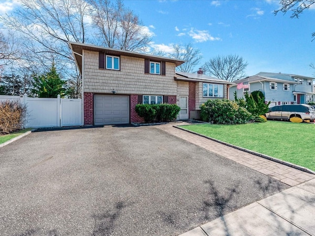 tri-level home with fence, an attached garage, a front lawn, aphalt driveway, and brick siding