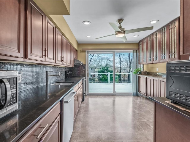 kitchen with appliances with stainless steel finishes, dark stone counters, wall chimney range hood, and a sink