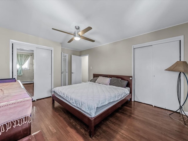 bedroom with a baseboard heating unit, wood finished floors, two closets, and a ceiling fan