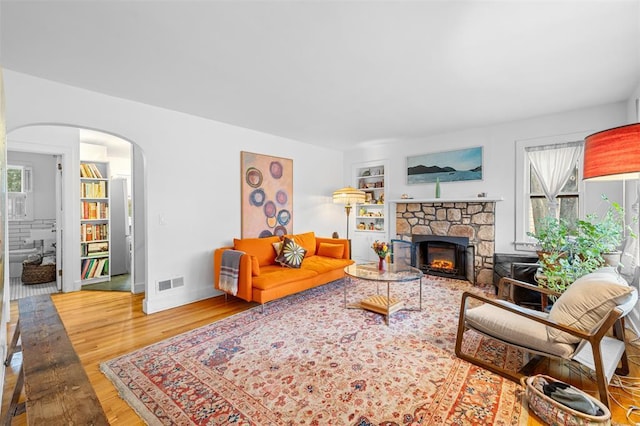 living area with visible vents, built in features, a fireplace, wood finished floors, and arched walkways