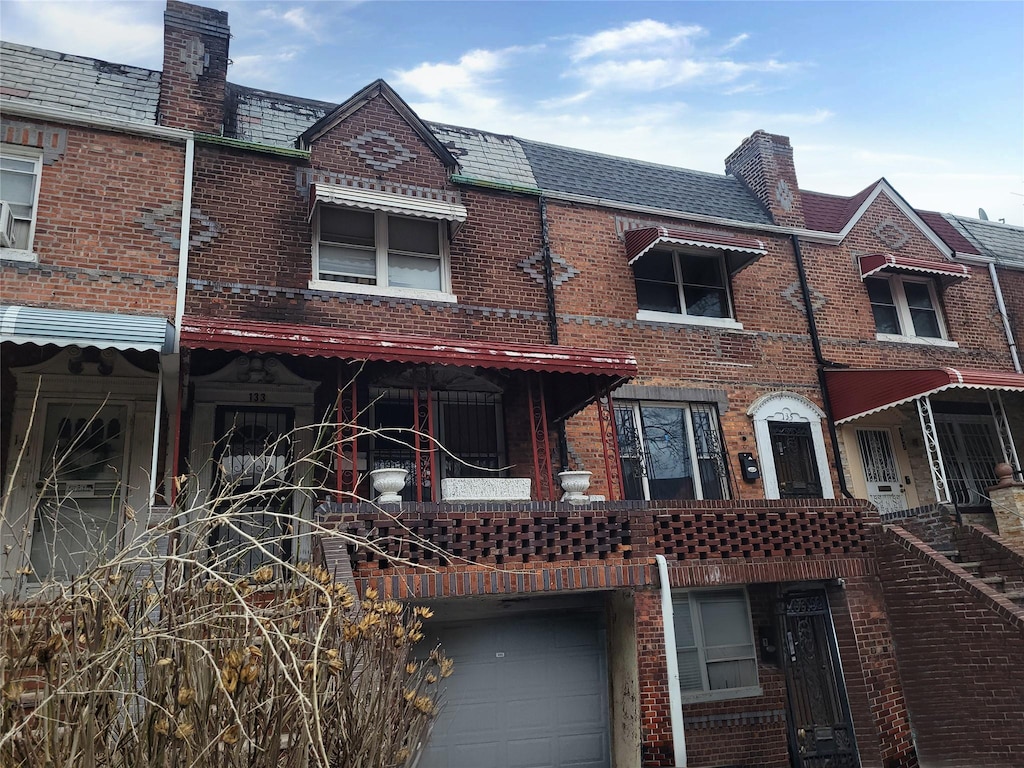 back of property featuring brick siding, mansard roof, and a high end roof