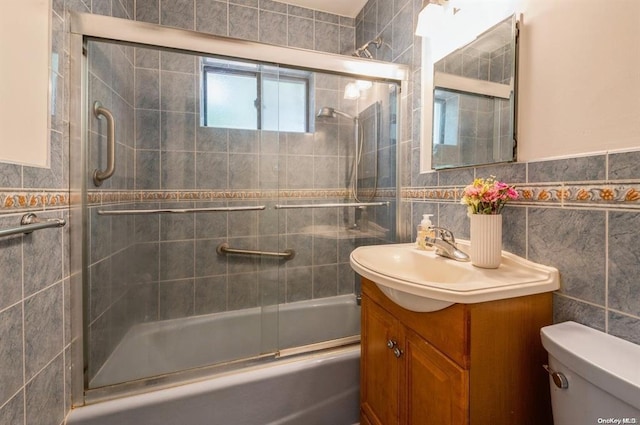 bathroom with tile walls, toilet, wainscoting, combined bath / shower with glass door, and vanity