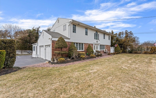 view of side of home featuring brick siding, fence, driveway, a yard, and an attached garage