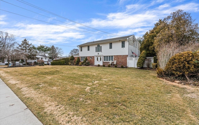 colonial inspired home featuring brick siding, a front lawn, and fence