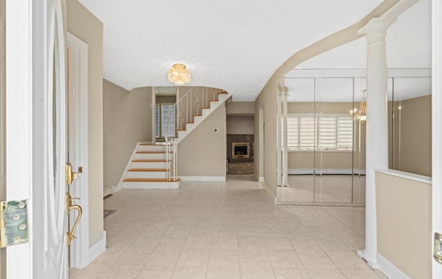 foyer entrance with baseboards, stairway, tile patterned floors, a fireplace, and a notable chandelier