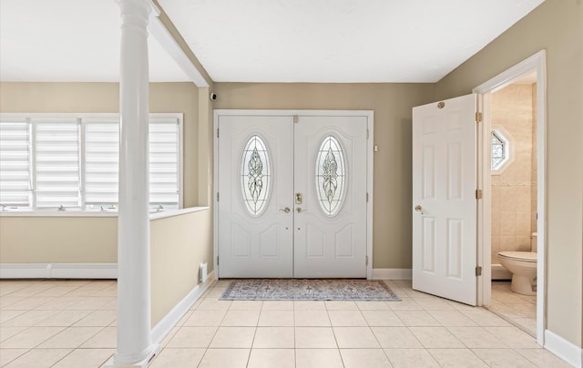 foyer with light tile patterned floors, baseboards, and ornate columns