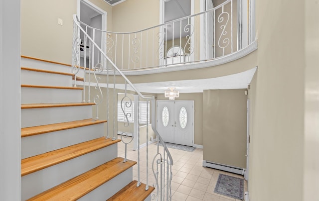 staircase featuring a baseboard heating unit, tile patterned flooring, a high ceiling, and baseboards