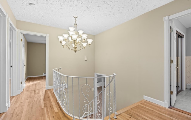 hall with light wood-style floors, a textured ceiling, and an upstairs landing