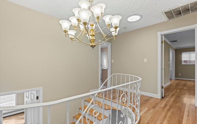 staircase with visible vents, hardwood / wood-style floors, baseboard heating, an inviting chandelier, and baseboards