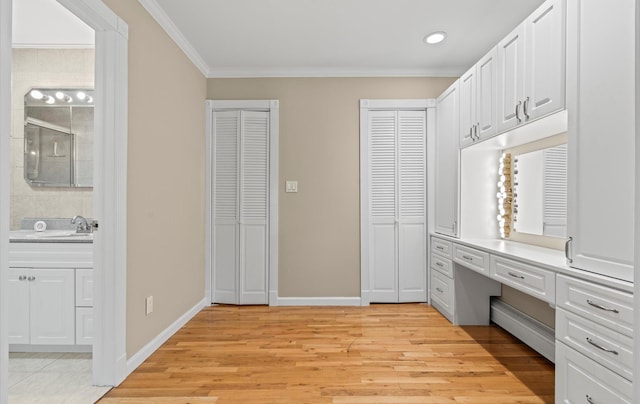 interior space with light wood-type flooring, baseboard heating, a sink, and built in study area