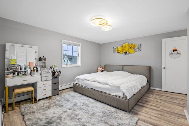 bedroom with baseboard heating, baseboards, and wood finished floors