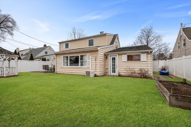 rear view of property with a garden, a lawn, and a fenced backyard