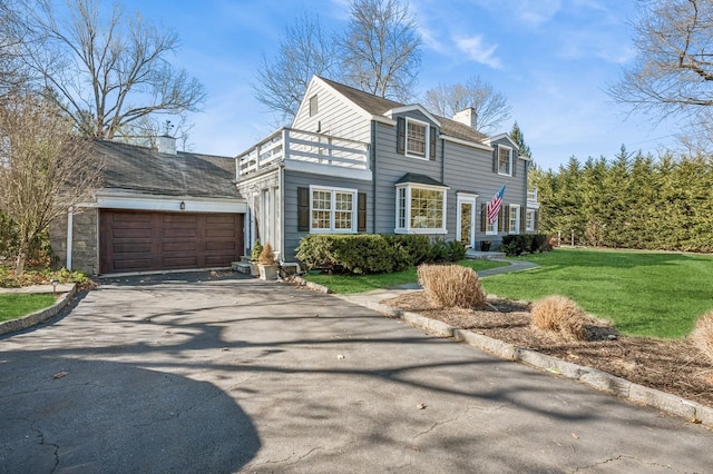 view of front of house with a front yard, a balcony, an attached garage, a chimney, and aphalt driveway