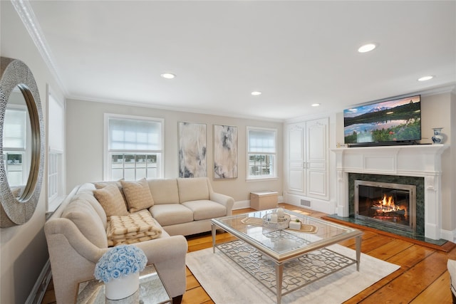 living room with a high end fireplace, plenty of natural light, light wood-style floors, and crown molding