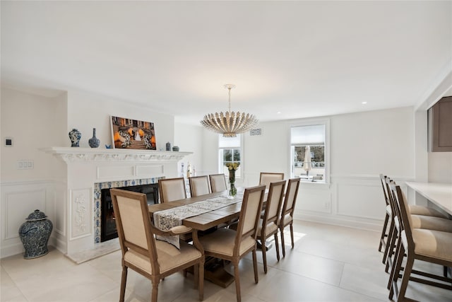 dining area with a chandelier, a premium fireplace, light tile patterned floors, wainscoting, and a decorative wall