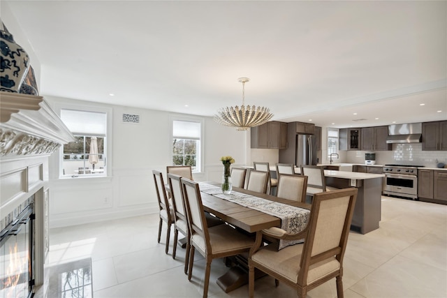 dining room featuring a tiled fireplace, wainscoting, recessed lighting, light tile patterned flooring, and a decorative wall