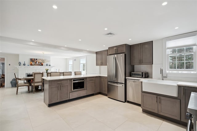 kitchen featuring a sink, appliances with stainless steel finishes, a peninsula, light countertops, and decorative backsplash