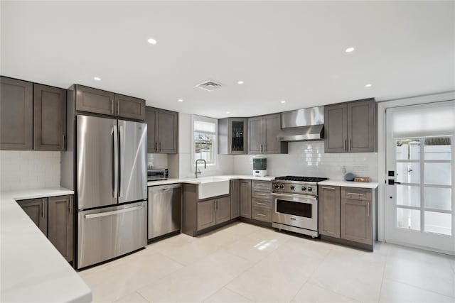 kitchen with visible vents, a sink, light countertops, appliances with stainless steel finishes, and wall chimney range hood