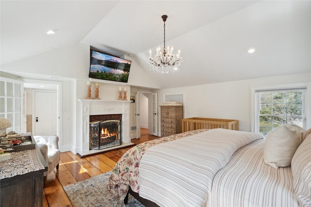 bedroom with lofted ceiling, a notable chandelier, a glass covered fireplace, and light wood finished floors