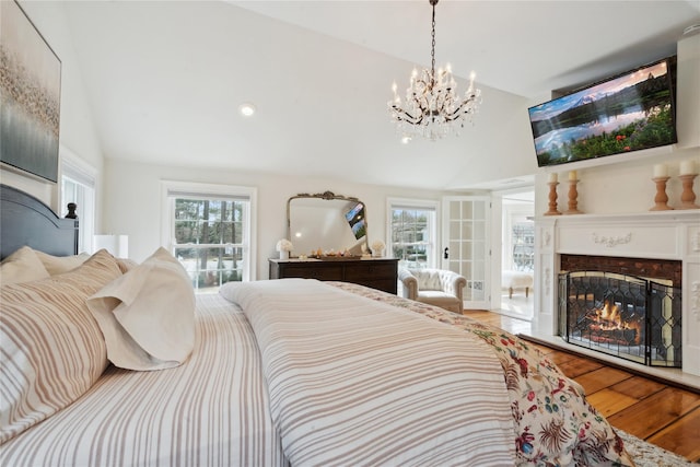 bedroom featuring multiple windows, high vaulted ceiling, a lit fireplace, and wood finished floors